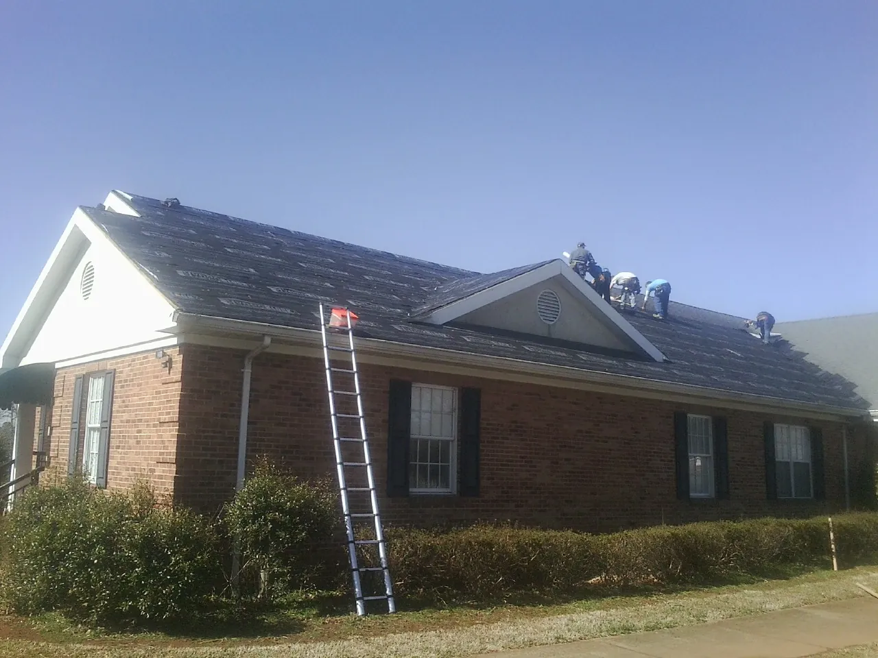 Crew tearing shingles off a brick ranch roof with a ladder set — Emergency Roof Repair work by our crew in Niles