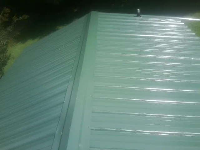 New green metal panels meeting at the ridge of a roof — Flat Roof Repair work by our crew in Niles