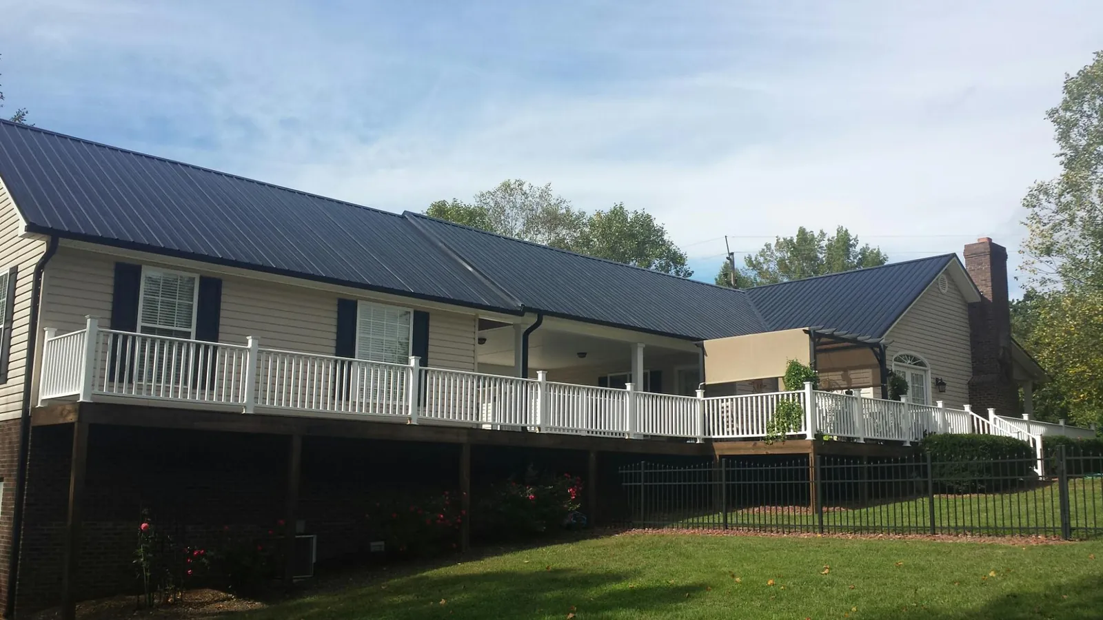 Black metal roof above a long white railed deck on a hillside home in Niles